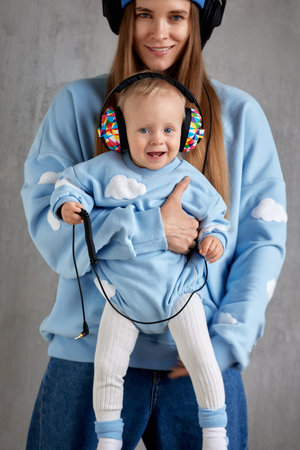 Happy young mother holds and hugs her smiling baby. The baby and mom wear similar blue clothes and...