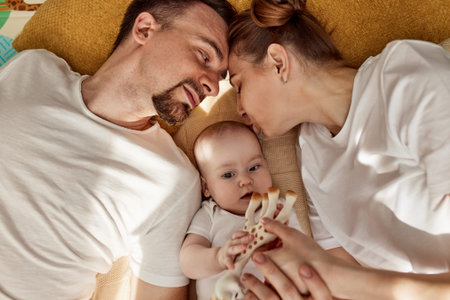 A cute joyful baby and his parents lie on the floor in a bright cozy room with toys. Mom and dad hug...