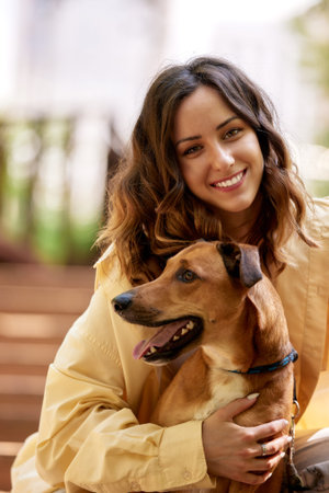 Charming young smiling girl walks with a dog of golden color in the park on a sunny day. The girl hugs her pet. Love and affection between owner and pet. Raising pets taken from a shelter. Close-up.の写真素材