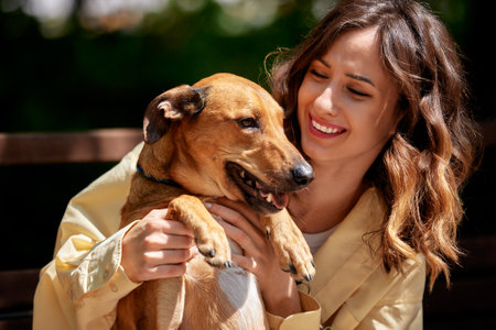 Charming young smiling girl with a dog of golden color on a walk in the park on a sunny day. The girl plays with her pet. Love and affection between owner and pet. Adopting a pet from a shelter.の写真素材