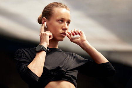 A cute young fitness girl takes out wireless headphones from a case and puts them in the ears....