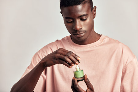 Young black guy holding a vial of facial mask cream in his hands before applying it on his face...