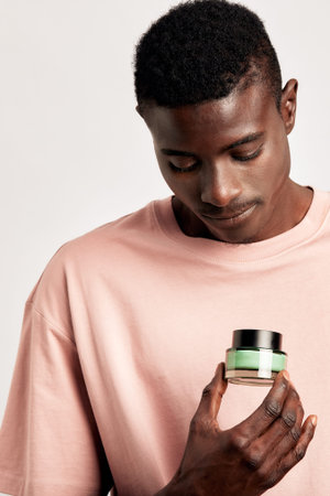 Young African American man holds a jar of moisturizing skin balm in his hand. Handsome black...