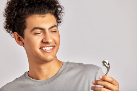 Young handsome smiling guy using de-puffing face roller to keep his skin soft and smooth. Swarthy man with black curly hair maintaining his natural beauty with skincare routine. Mens self-care.の写真素材