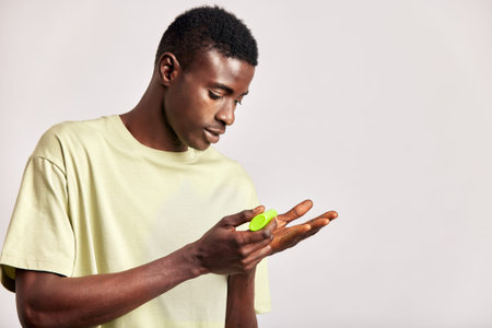 Young handsome black guy holds bottle of facial wash or beauty cream preparing to apply it on his...