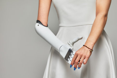 Cropped studio portrait of a young girl with disability wearing sensory bionic prosthetic arm. Beautiful slender woman in a white dress fully controls her artificial robotic hand.の写真素材