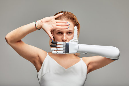 Studio portrait of a young girl with disability wearing sensory bionic prosthetic arm. Beautiful woman folded her hands in a frame in front of her face fully controlling her artificial robotic hand.の写真素材