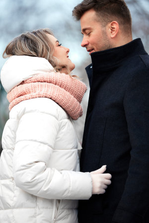 Happy couple in love in winter park. Young beautiful man and woman in winterwear embracing and looking at each other with tenderness. Romantic winter outside date.の写真素材