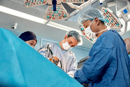Low angle shot of surgeons team during complex surgical operation in a bright sterile operating...