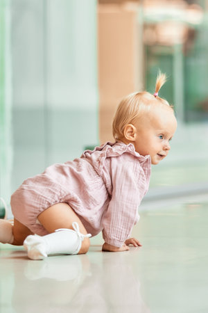 Small cute child crawling on the floor in a public place, shopping mall. Tiny blonde girl in pink...