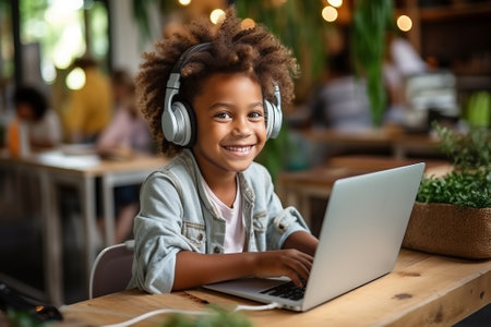 Kid with headphones is sits at table and studies at home online while uses laptop, listens online tutor or audio course. Homeschoolingの素材
