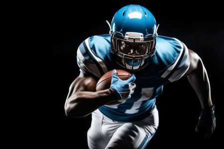 Portrait of American football player running with the ball. Muscular athlete in a blue and white uniform with an ovoid ball in a dynamic pose. Isolated on black background.の素材