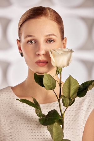 Portrait of a beautiful young disabled woman, born without an arm, holding a flower in her hands in a white dress. Diversity disability and flowers.の写真素材
