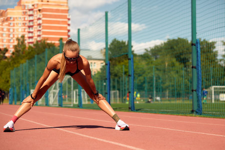 Young woman runner warming up at the racetrack. Fit runner workout, stretch her muscle and warming...