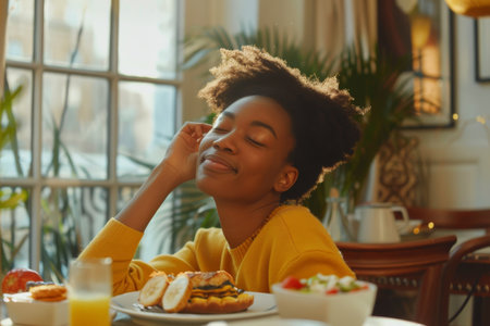 Young black woman enjoying a sunny morning breakfast indoorsの素材