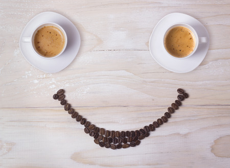 Two cups of coffee with beans smile on white wood tableの写真素材
