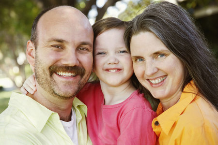 Mother and father hold their daughter between them as all three smile for the camera. Horizontal...