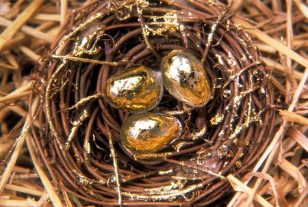 Overhead view of a woven nest sitting in straw with three golden eggs. Horizontal shot.の写真素材