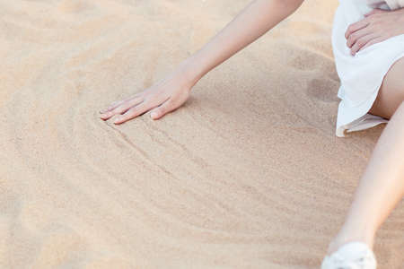 Girl sitting on the beach wipes the sand by handの写真素材