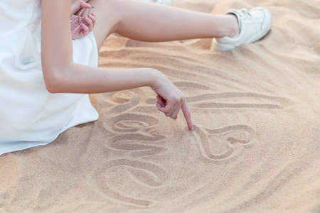 Girl sitting on the beach is writing loveの写真素材