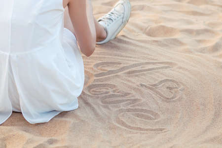 Girl sitting on the beach writes down loveの写真素材
