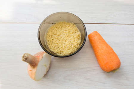 onions,carrots and a Cup of dry pasta on wooden tableの写真素材