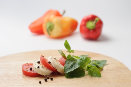 slices of mozzarella and tomato, decorated with  fresh oregano, with peppers in teh background, on whiteの写真素材