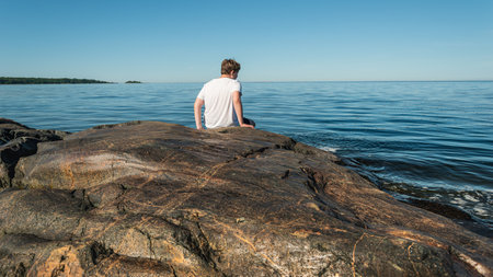A teenager sits on the rocks and looks out over the Swedish Baltic Sea on a beautiful summer day but cannot swim due to the algae bloom in the sea. Sweden ÃngskÃ¤r sea camping 24 July 2019のeditorial素材