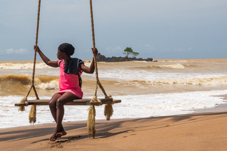 African woman sitting by the sea on a hanging chair. Axim Ghana West Africa Beach 2018 November 2のeditorial素材