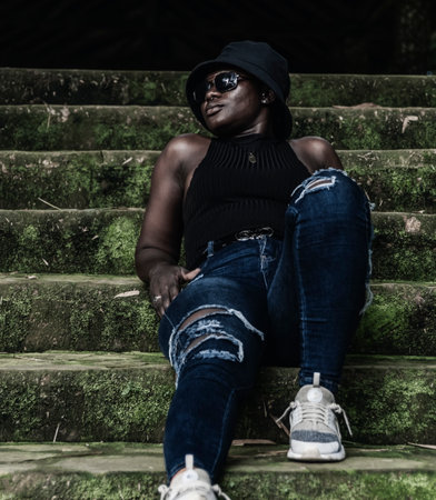 African young woman with hat sitting on an old staircase in the jungle Ghana West Africaの写真素材