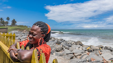 Happy African woman hangs over a fence at the sea coast in Ghana Takoradi West Africaの写真素材