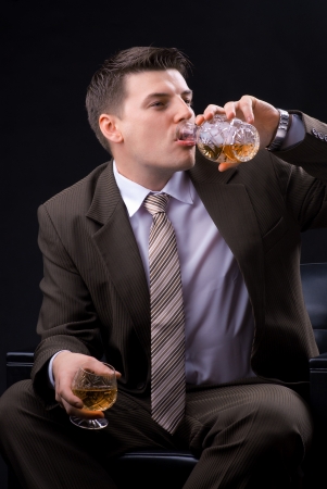 Young businessman sitting on a couch with an alcoholic beverage の写真素材