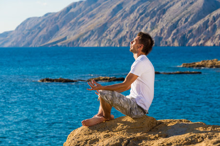Handsome man in a yoga position on the beachの写真素材