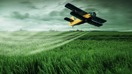 A crop dusting plane working over a fieldの素材 [FY31028450749]