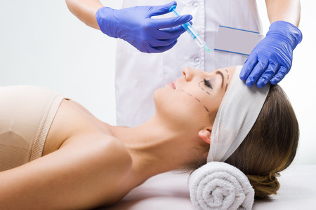 Beautiful woman lying in the clinic, a plastic surgeon in the hands of the needle の写真素材