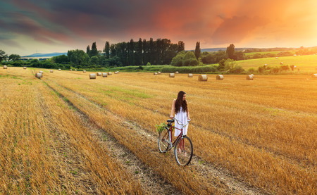 Beautiful woman pushes old red bike in a wheat fieldの写真素材