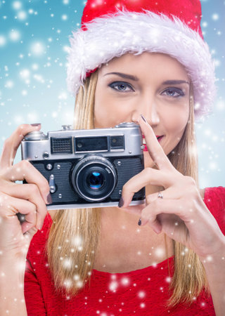 Beautiful woman with santa hat, holding the camera - snowfallの写真素材
