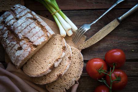 Fresh brown bread on a wooden plate with vegetablesの写真素材