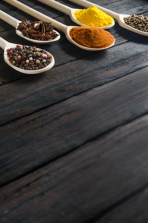 different spices in wooden spoons on a black wooden background like Pepper, coriander, dried vegetables and otherの写真素材