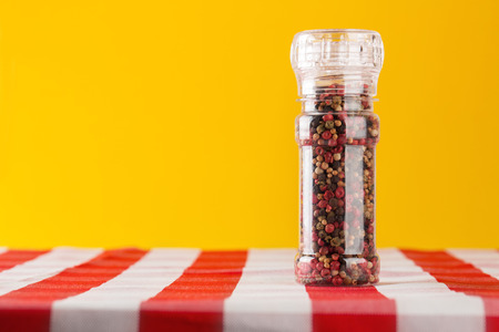 Colored Peppers Mix and pepper grinder in the kitchen table on yellow backgroundの写真素材