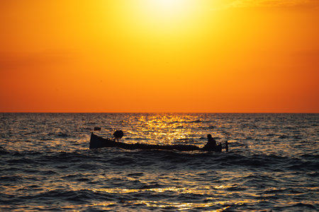 Fisherman sailling with his boat on beautiful sunrise over the seaの写真素材