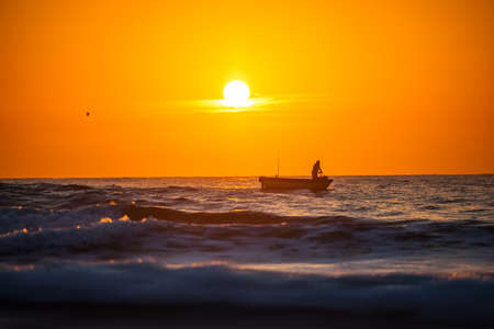 Fisherman sailling with his boat on beautiful sunrise over the seaの写真素材