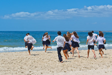 School's out. On their very last day of school - high school students in their school uniforms running traditionally into the oceanのeditorial素材