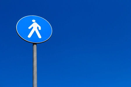 A sign of European pedestrian crossing, isolated on blue sky background.