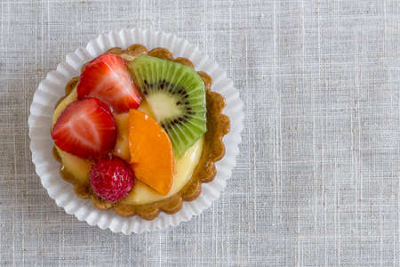 A cake with cream and mixed fruit, resting on linen tablecloth.の写真素材