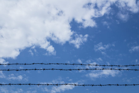 Barbed wire fence with blue sky and clouds in the background.の写真素材