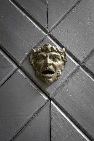 Front view of a door decorated with a face sculpted in bronze.