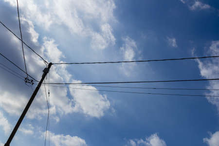 Old wooden pole with cables for telephone and power services with blue and cloudy skyの写真素材