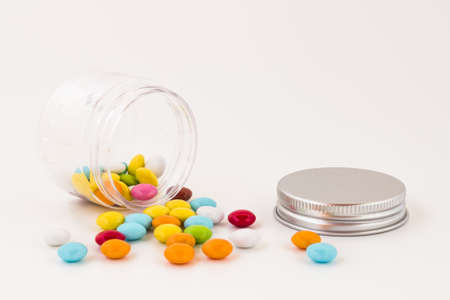 Colored smarties scattered out of an open glass jar, isolated on white background. Shallow depth of field.の写真素材