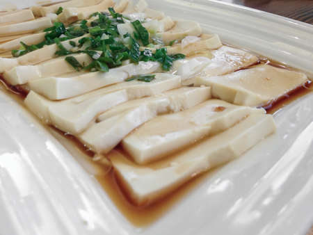 Plate of tofu slices with parsley, onions and soy sauce. Shallow depth of field.の写真素材
